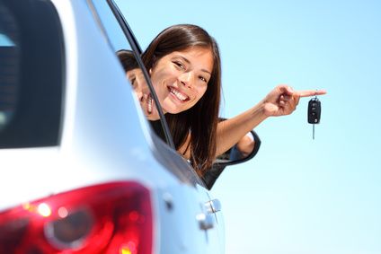 Smiling driver holding up car keys from her vehicle window after car key replacement